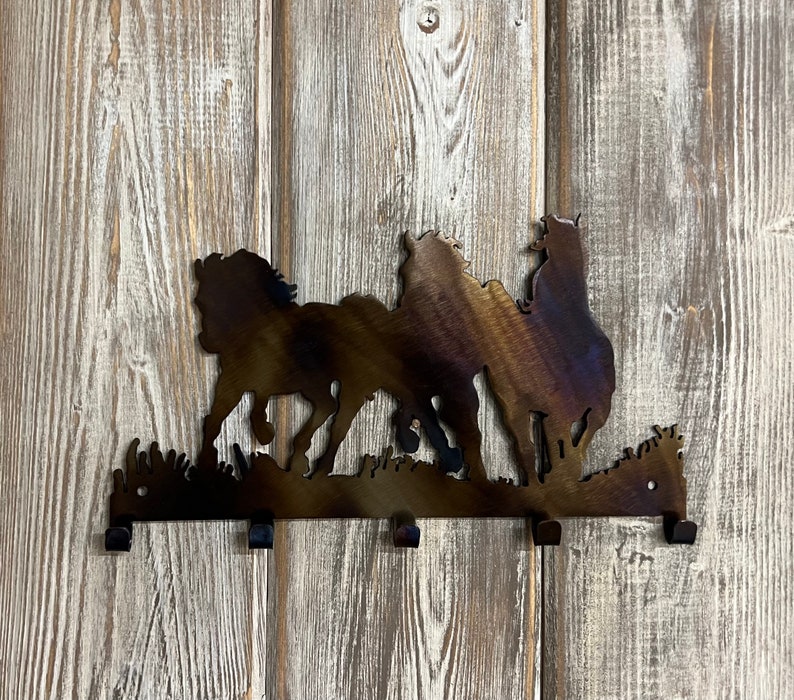 May include: Metal wall mounted key holder with a silhouette of three horses running. The key holder has five hooks.