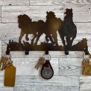 May include: Metal key holder with a silhouette of three horses running. The key holder has five hooks for hanging keys.