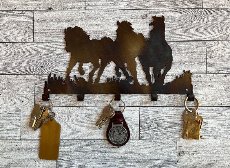 May include: Metal key holder with a silhouette of three horses running. The key holder has five hooks for hanging keys.
