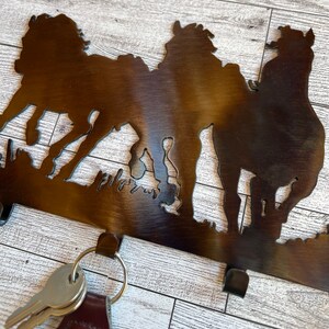 May include: Metal key holder with a silhouette of three horses. The key holder has three hooks for hanging keys.