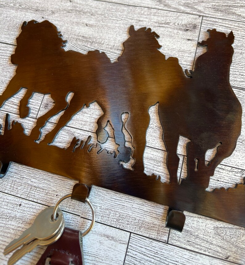 May include: Metal key holder with a silhouette of three horses. The key holder has three hooks for hanging keys.