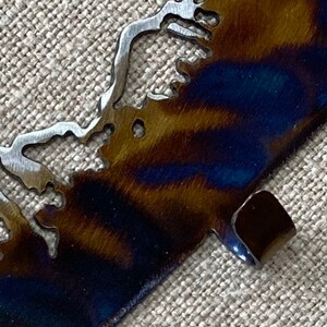 May include: A metal cutout of a coastline with a blue and brown patina finish. The cutout has a small tab on the bottom right corner.