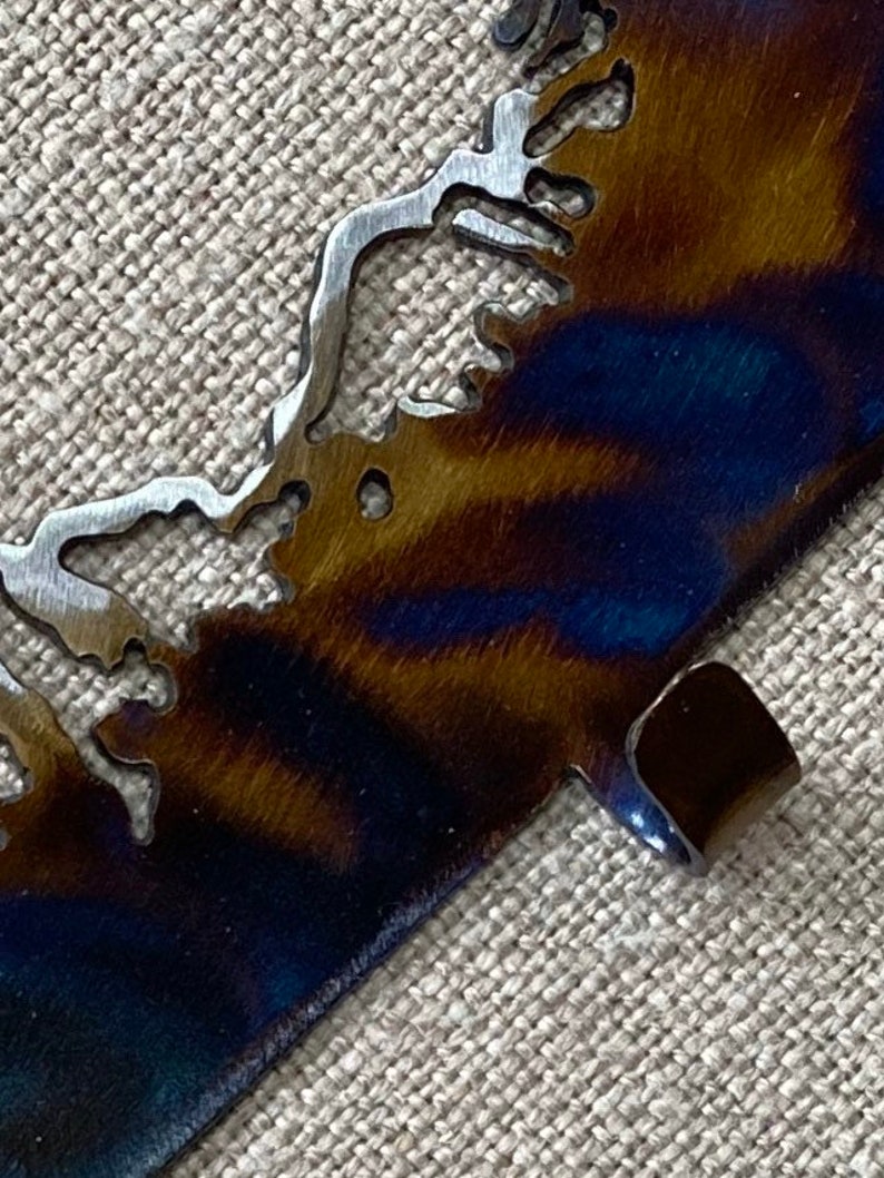 May include: A metal cutout of a coastline with a blue and brown patina finish. The cutout has a small tab on the bottom right corner.