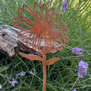 May include: A rusty metal sunflower garden stake with a detailed design. The stake is placed in a bed of purple lavender flowers.