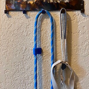 May include: A metal wall hook with a mountain range silhouette design. Two leashes, one blue and white rope and one beige nylon, are hanging from the hooks.