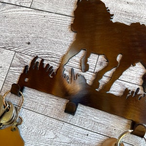 May include: A metal key holder shaped like a running dog silhouette. The holder has four hooks and is mounted on a white wood surface. Keys are hanging from the hooks.