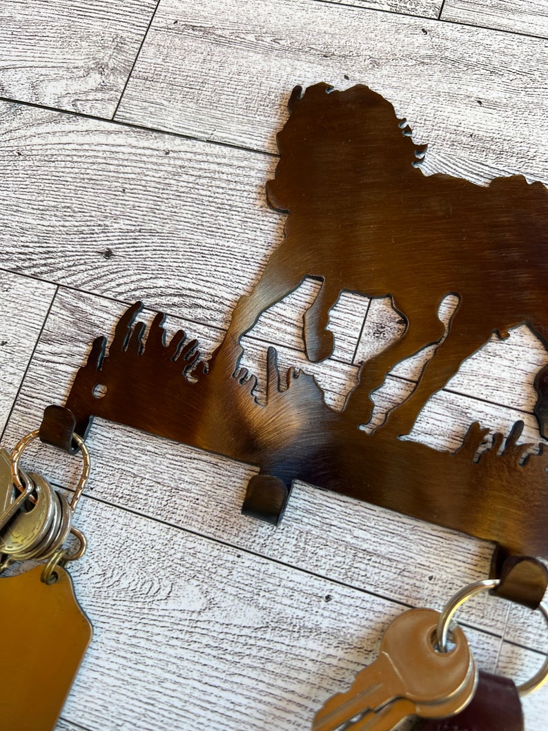 May include: A metal key holder shaped like a running dog silhouette. The holder has four hooks and is mounted on a white wood surface. Keys are hanging from the hooks.