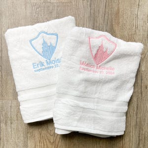 May include: Two white towels with embroidered blue and pink shields. The shields feature a building and the text "Erik Mois septembre 22." and "Mónica Michelle Septiembre 22, 2024".