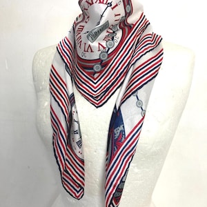 May include: A white scarf with a red, white, and blue clock design. The scarf features a repeating pattern of clocks and stripes, with the word "Piramit" visible on the clock face. The scarf is draped over a mannequin.