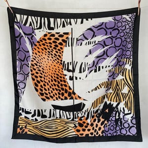 Può includere: Foulard quadrato in seta con un design astratto audace. La sciarpa presenta un bordo nero, uno sfondo bianco e una barca a vela con una vela arancione. Il design incorpora motivi animalier viola, neri e gialli.