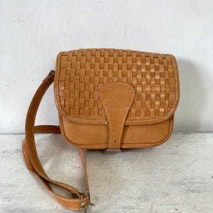 Bolso de cuero vintage estilo sillín, con patrón trenzado en color tostado y cierre de hebilla, estilo bohemio hippie.