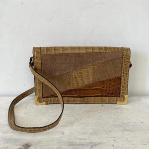 Op de afbeelding: Een bruine leren schoudertas met een patchwork-ontwerp. De tas heeft een gouden sluiting en een lange band.