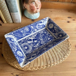 May include: A rectangular ceramic tray featuring a blue and white pattern with celestial motifs including suns, moons, stars, and clocks. The text "CELEBRATE" and "MILLENNIUM" is printed along the edges of the tray, which has a white base and blue illustrations.
