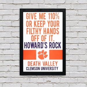 May include: A black framed poster with an orange and white background. The poster says "Give me 110% or keep your filthy hands off of it. Howard's Rock. Death Valley. Clemson University." with a purple paw print in the center.