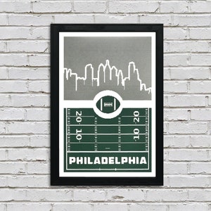 May include: A green and gray print featuring a stylized cityscape of Philadelphia, Pennsylvania, with a football field and a football in the center. The text "PHILADELPHIA" is printed below the field.