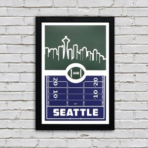 May include: A green and blue football field print with a white silhouette of the Seattle skyline, including the Space Needle, and the word "SEATTLE" in white text.