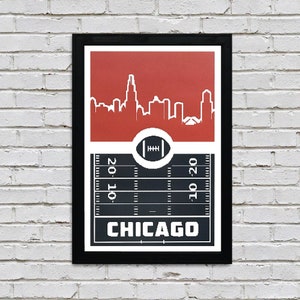 Puede incluir: Una impresión enmarcada en negro con un fondo rojo que presenta una silueta blanca del horizonte de Chicago. La parte inferior de la impresión presenta un campo de fútbol negro y blanco con la palabra "CHICAGO" en texto blanco.