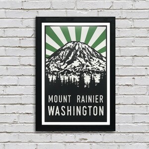May include: A black framed poster with a vintage style illustration of Mount Rainier in Washington state. The mountain is depicted in black and white with a green sunburst behind it. The text "MOUNT RAINIER WASHINGTON" is printed in white at the bottom of the poster.