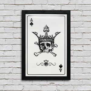 May include: A black and white illustration of a playing card, the Ace of Spades. The card features a skull wearing a crown and crossed bones. The card is framed in a black frame.