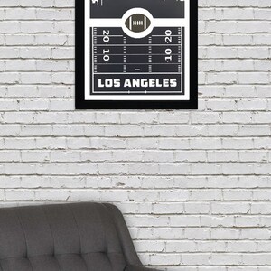 May include: Black and white framed print of a football field with a city skyline above it. The text "LOS ANGELES" is below the field. The field has yard lines and a football in the center.