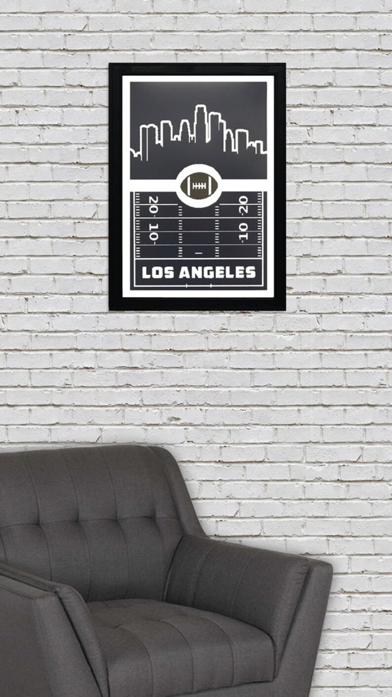 May include: Black and white framed print of a football field with a city skyline above it. The text "LOS ANGELES" is below the field. The field has yard lines and a football in the center.