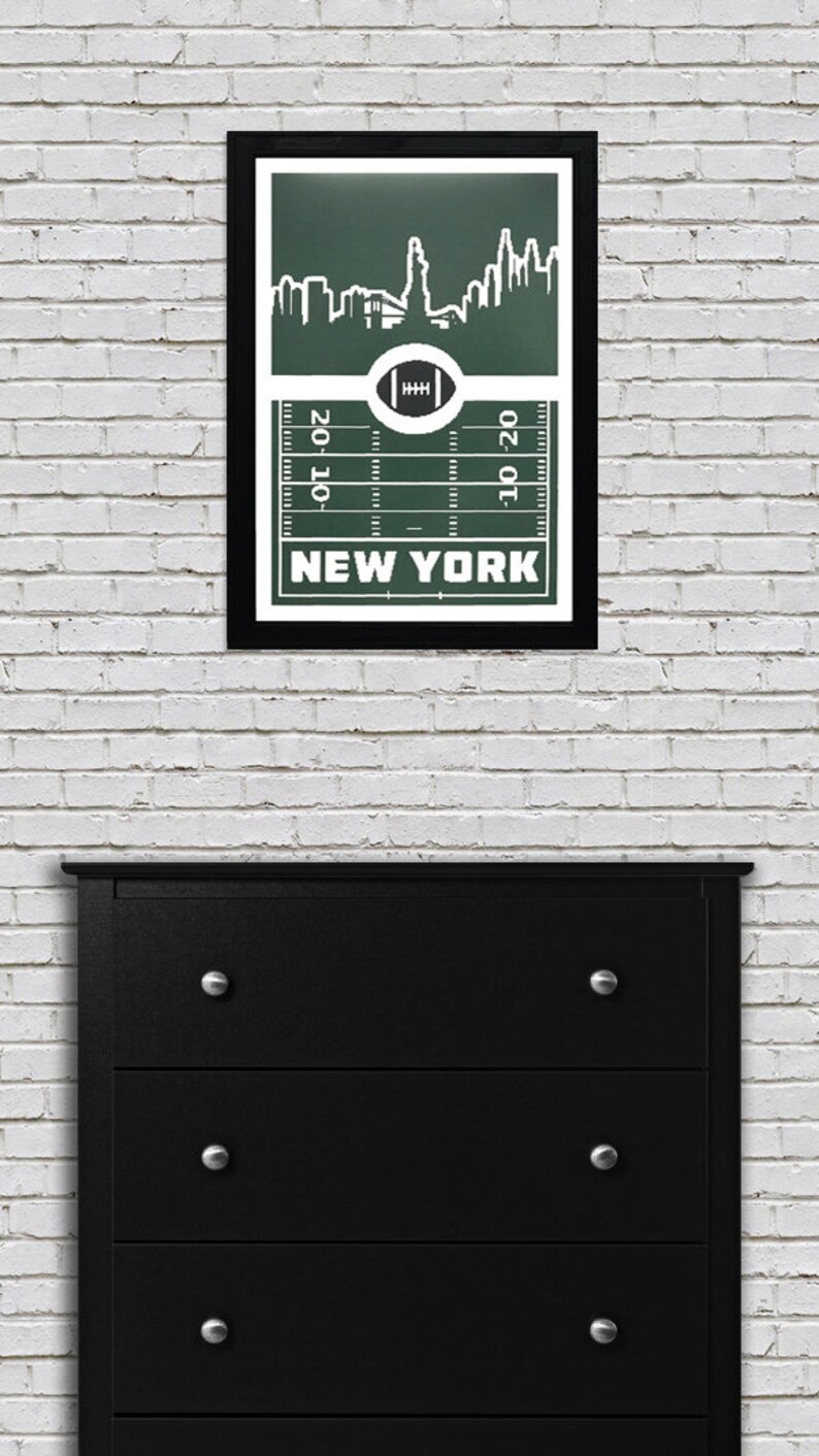 Puede incluir: Una impresi&oacute;n enmarcada con un fondo verde que presenta una silueta blanca del horizonte de la ciudad de Nueva York. El horizonte est&aacute; sobre un campo de f&uacute;tbol con las palabras "NEW YORK" impresas debajo del campo.