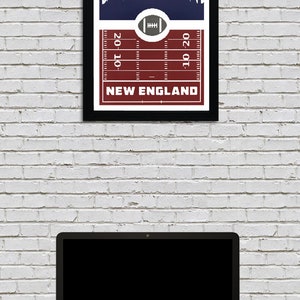 May include: A framed print with a navy blue background featuring a white silhouette of a city skyline. The bottom of the print has a red and white football field design with the text "NEW ENGLAND" and yard lines marked "20", "10", and "10-20".
