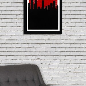 May include: A framed art print featuring the Denver skyline in black against a red background. The word "DENVER" is displayed in white, above "THE MILE HIGH CITY". The print is in a black frame, hanging on a white brick wall.
