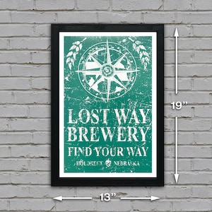 May include: A framed poster with a distressed green background and white text. The poster features a compass with a white star and the text "Lost Way Brewery Find Your Way" with the location "Hildreth, Nebraska". The poster is 13 inches wide and 19 inches tall.