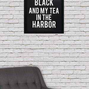 May include: Black and white framed print with the text "I like my coffee black and my tea in the harbor" hanging on a white brick wall above a gray armchair.