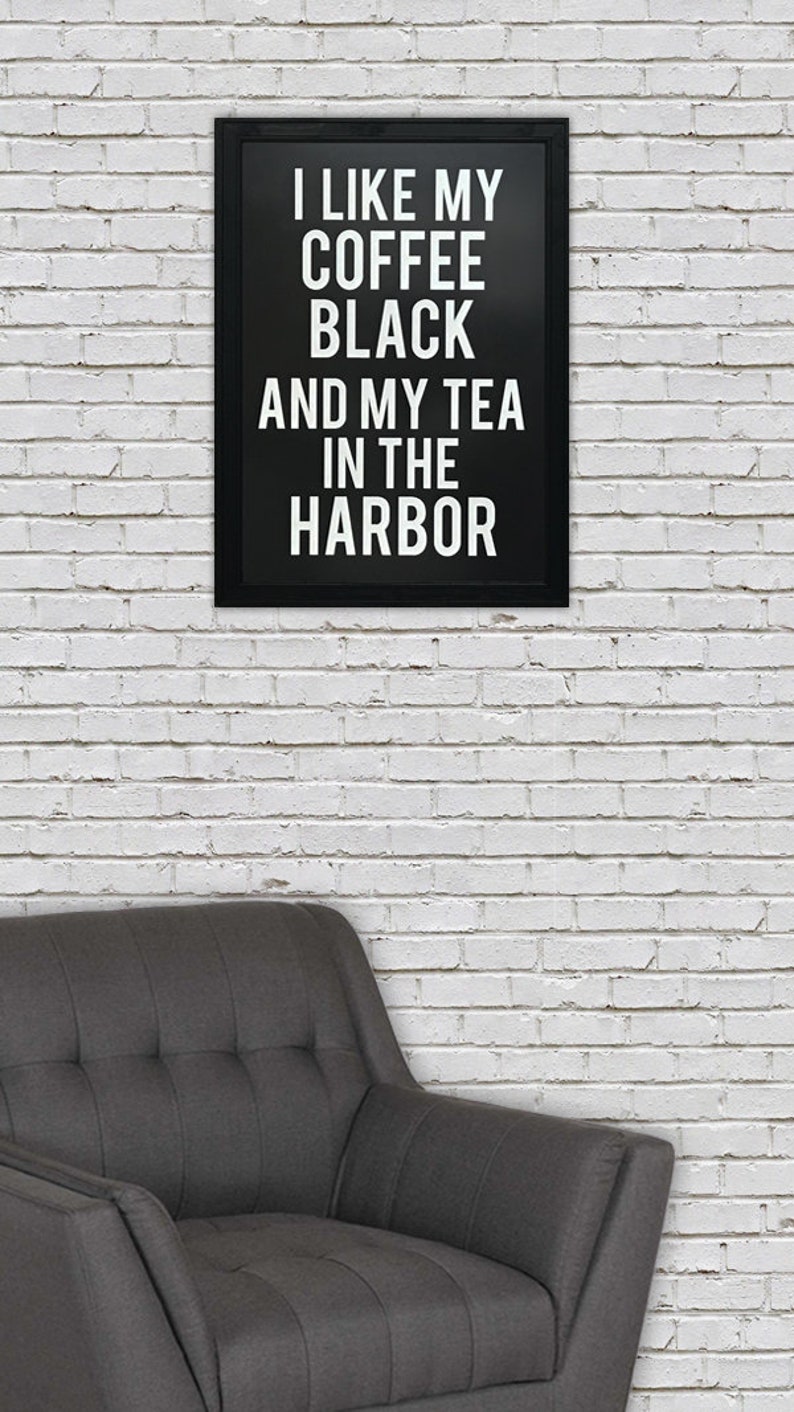 May include: Black and white framed print with the text "I like my coffee black and my tea in the harbor" hanging on a white brick wall above a gray armchair.