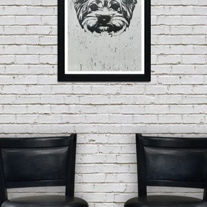 May include: A black and white framed print of a dog's face. The dog has long fur and is looking directly at the camera. The print is hanging on a white brick wall between two black bar stools.