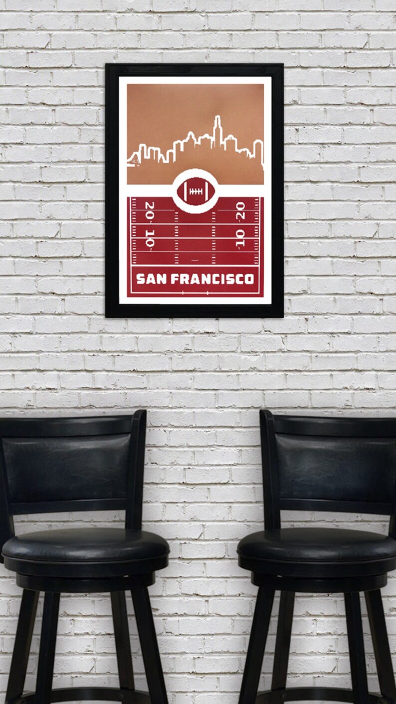 May include: A framed print of a white silhouette of the San Francisco skyline against a brown background. The skyline is set against a red football field with yard lines and a football in the center. The text "SAN FRANCISCO" is printed below the field.