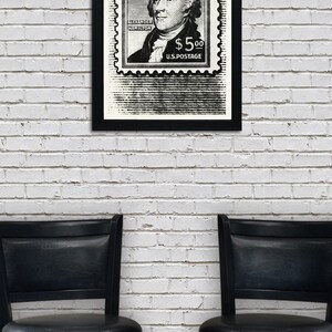 May include: A black and white framed print of a vintage postage stamp featuring a portrait of Alexander Hamilton with the text "ALEXANDER HAMILTON $5.00 U.S. POSTAGE". The print is hanging on a white brick wall between two black bar stools.