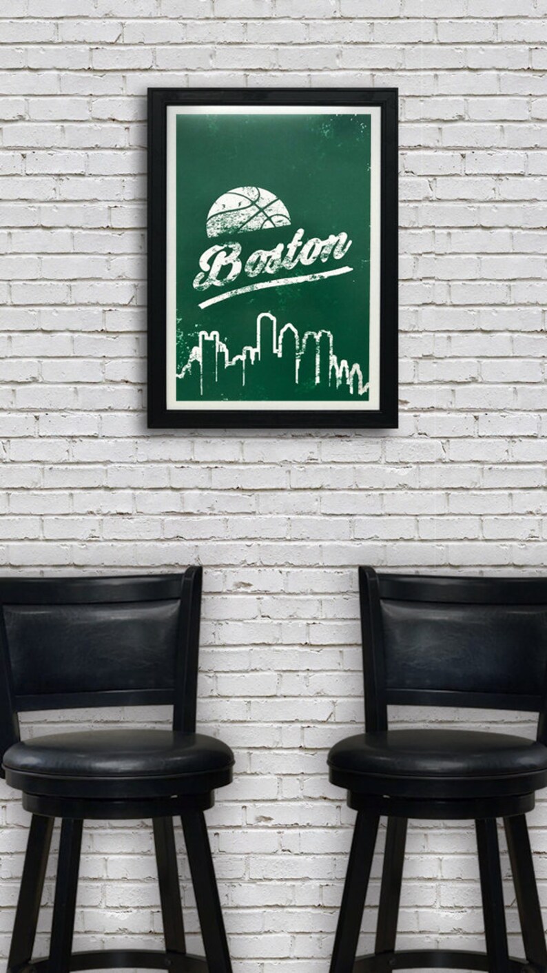 May include: A framed poster with a green background and white text that says "Boston". A basketball is above the text and a white silhouette of the Boston skyline is below the text. The poster is hanging on a white brick wall between two black bar stools.