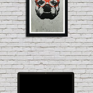 May include: A black and white illustration of a bulldog wearing red glasses. The illustration is framed in a black frame and hanging on a white brick wall. A laptop computer is sitting on a dark surface in front of the wall.