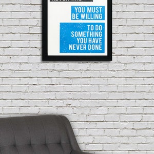 May include: A motivational quote in a black frame on a white brick wall. The quote reads: "If you want something you have never had, you must be willing to do something you have never done."