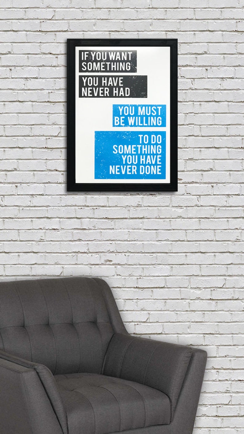 May include: A motivational quote in a black frame on a white brick wall. The quote reads: "If you want something you have never had, you must be willing to do something you have never done."