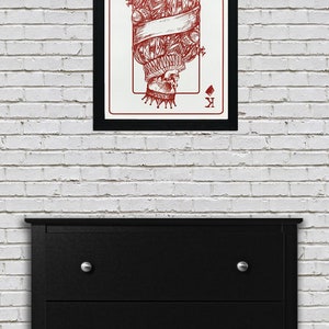 May include: A framed print of a playing card featuring a red skull king of diamonds. The skull is wearing a crown and is surrounded by a banner.