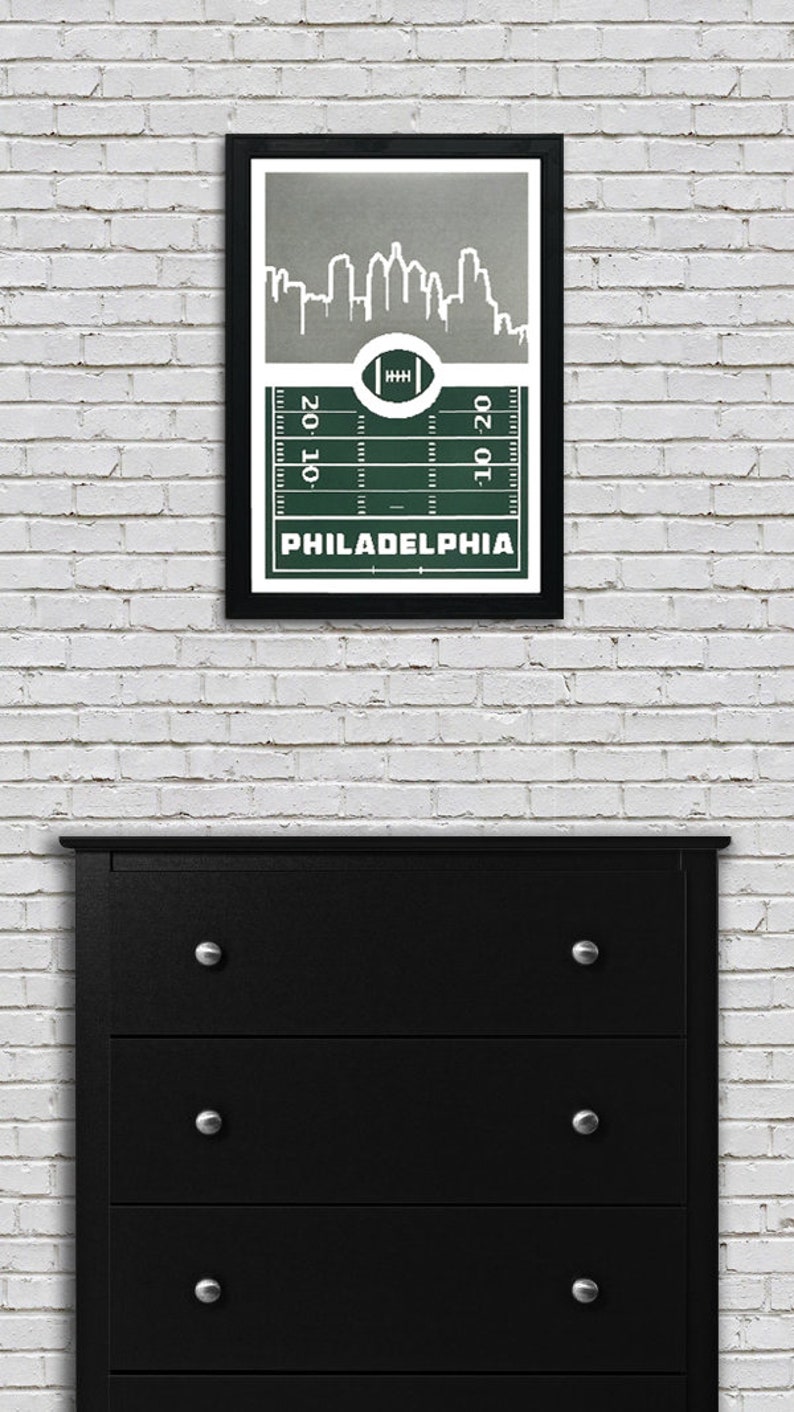 May include: A framed print of a green football field with a white outline of the Philadelphia skyline above it. The text "PHILADELPHIA" is printed below the field.