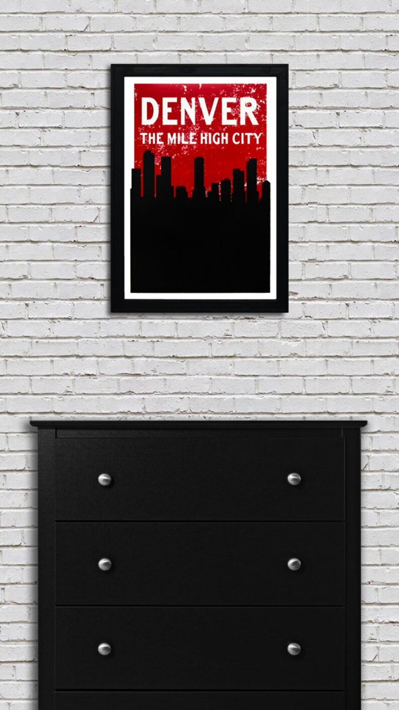 May include: A framed art print featuring the Denver skyline in black against a red background. The text "DENVER" and "THE MILE HIGH CITY" are displayed in white. The print hangs above a black dresser with silver knobs.