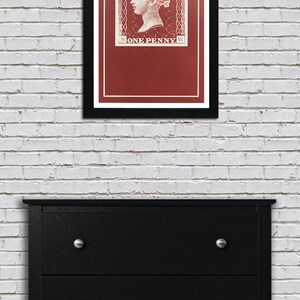 May include: A framed print of a vintage postage stamp featuring a portrait of Queen Victoria. The stamp is red with white lettering that reads "POSTAGE" and "ONE PENNY".