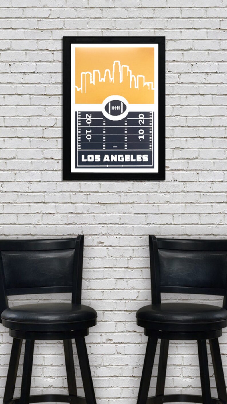 May include: A black framed print with a gold background featuring a white silhouette of the Los Angeles skyline. The bottom of the print shows a black and white football field with the text "LOS ANGELES" and the numbers "20-10" and "10-20".