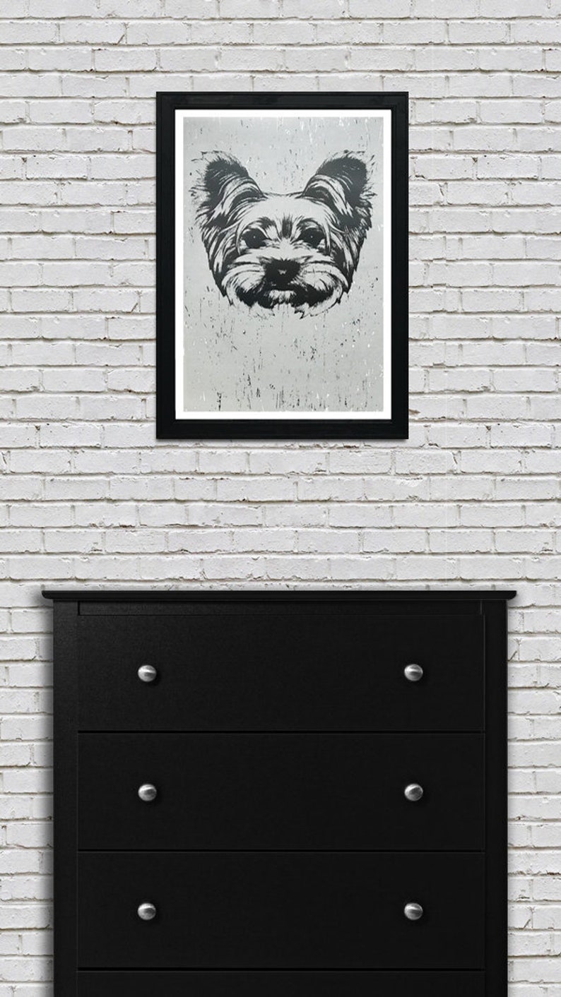 May include: Black and white illustration of a Yorkshire Terrier dog's face in a black frame on a white brick wall.