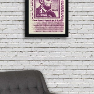 May include: A framed print of a vintage US postage stamp featuring a portrait of Abraham Lincoln. The stamp is purple and white and says "4&cent; U.S. POSTAGE" and "LINCOLN".