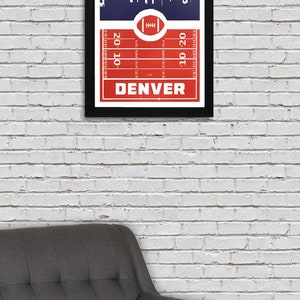 May include: A framed print with a red and white football field design. The print features a skyline of Denver, Colorado, and the text "DENVER" at the bottom.