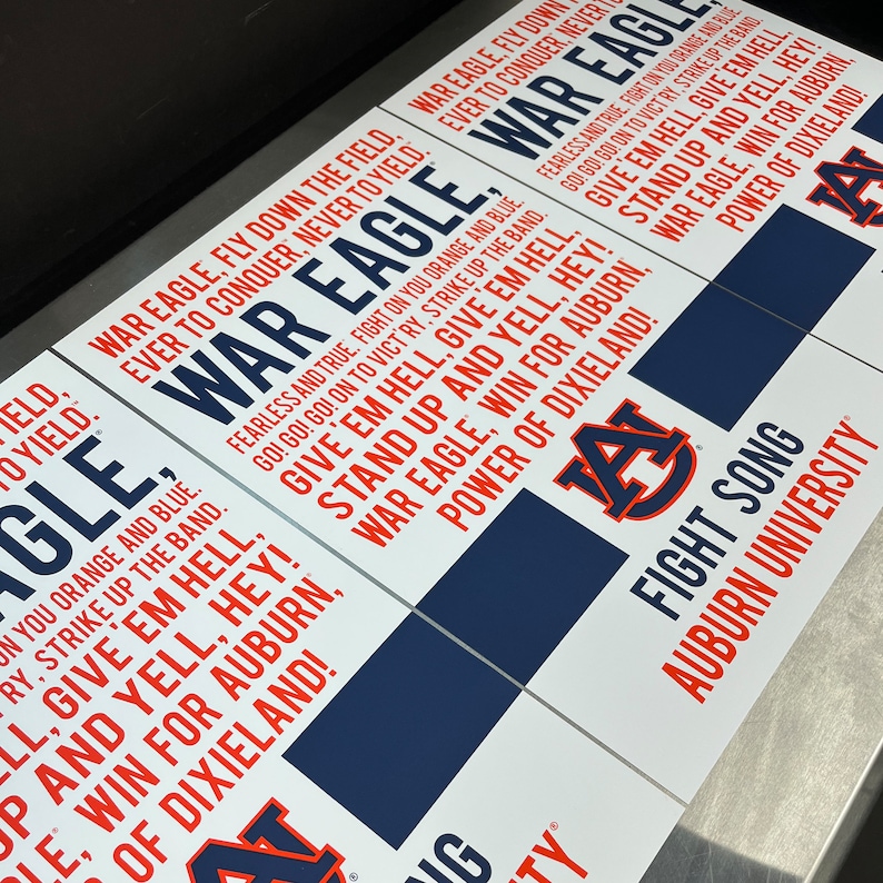 K&ouml;nnte beinhalten: Ein wei&szlig;es Schild mit blauem und rotem Text und einem blau-roten Logo. Der Text lautet "War Eagle, Fly Down the Field, Ever to Conquer, Never to Yield." Das Logo ist ein "A" mit einem roten "A" auf einem blauen "A". Der Text lautet auch "Give 'em Hell, Give 'em Hell, Stand Up and Yell, Hey! War Eagle, Win for Auburn, Power of Dixieland!" und "Fight Song, Auburn University".