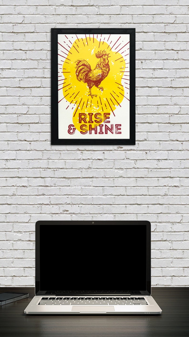 May include: A framed print with a yellow background and a red rooster illustration. The rooster is crowing and has a sunburst behind it. The text "RISE & SHINE" is below the rooster.