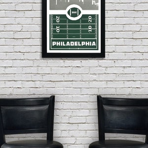 May include: A framed print of a green football field with a white outline of the Philadelphia skyline above it. The text "PHILADELPHIA" is printed below the field.
