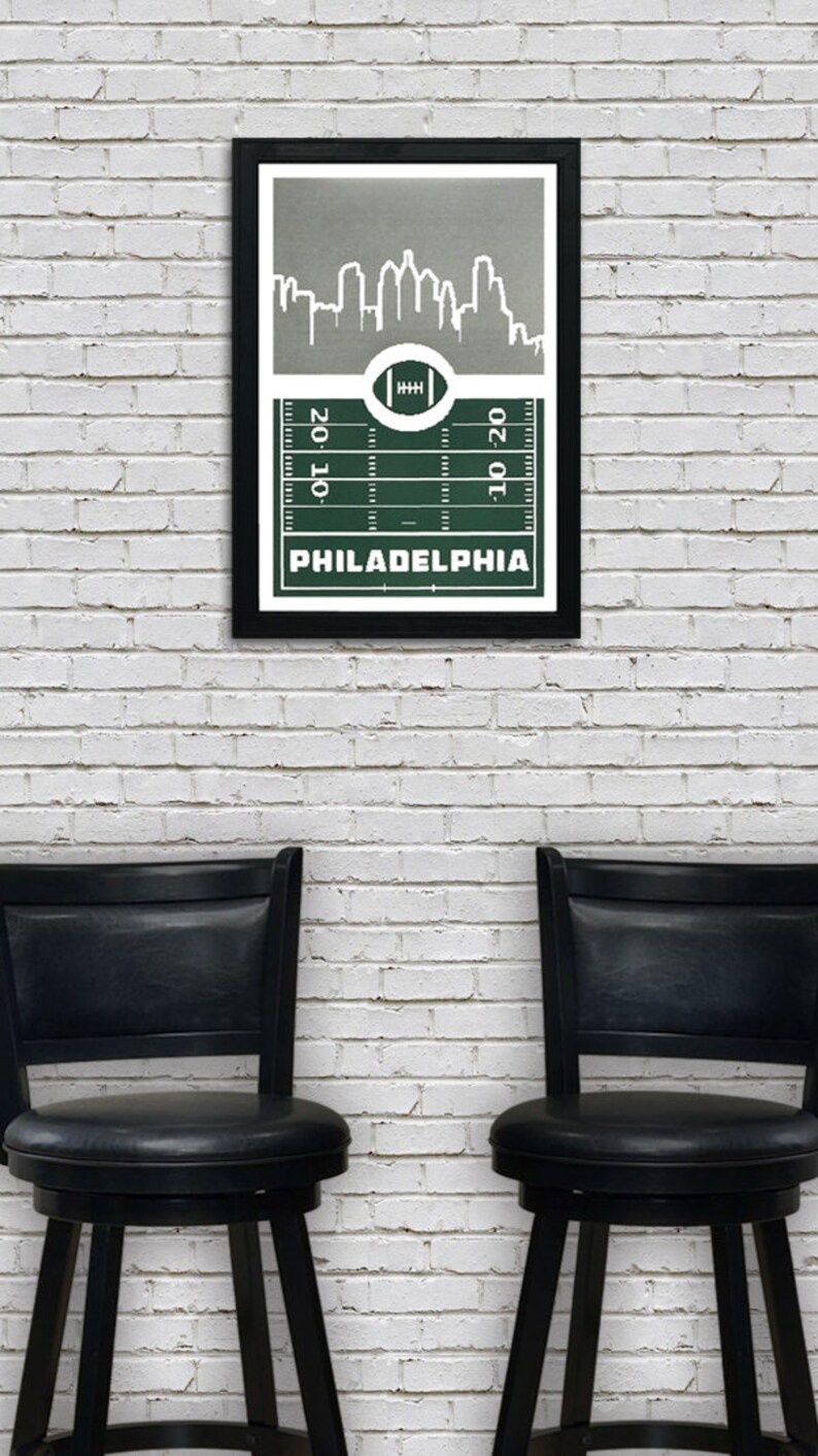 May include: A framed print of a green football field with a white outline of the Philadelphia skyline above it. The text "PHILADELPHIA" is printed below the field.